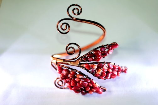 An intricately designed wire bracelet featuring swirling copper wires and clusters of red beads arranged in a floral pattern.