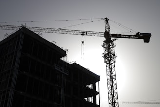 A panoramic view of a sprawling construction site at dawn with cranes silhouetted against the sky.