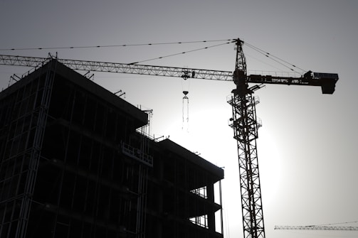A panoramic view of a sprawling construction site at dawn with cranes silhouetted against the sky.