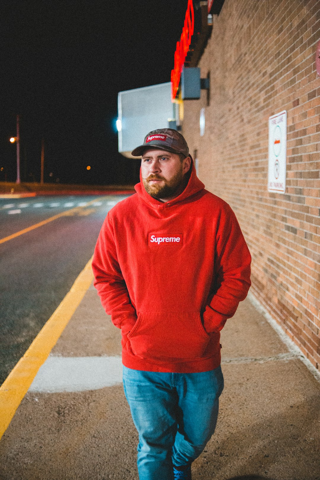 man in red hoodie standing on sidewalk during night time