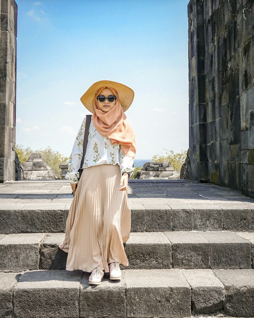 woman in brown long sleeve dress wearing brown sun hat standing on gray concrete stairs during