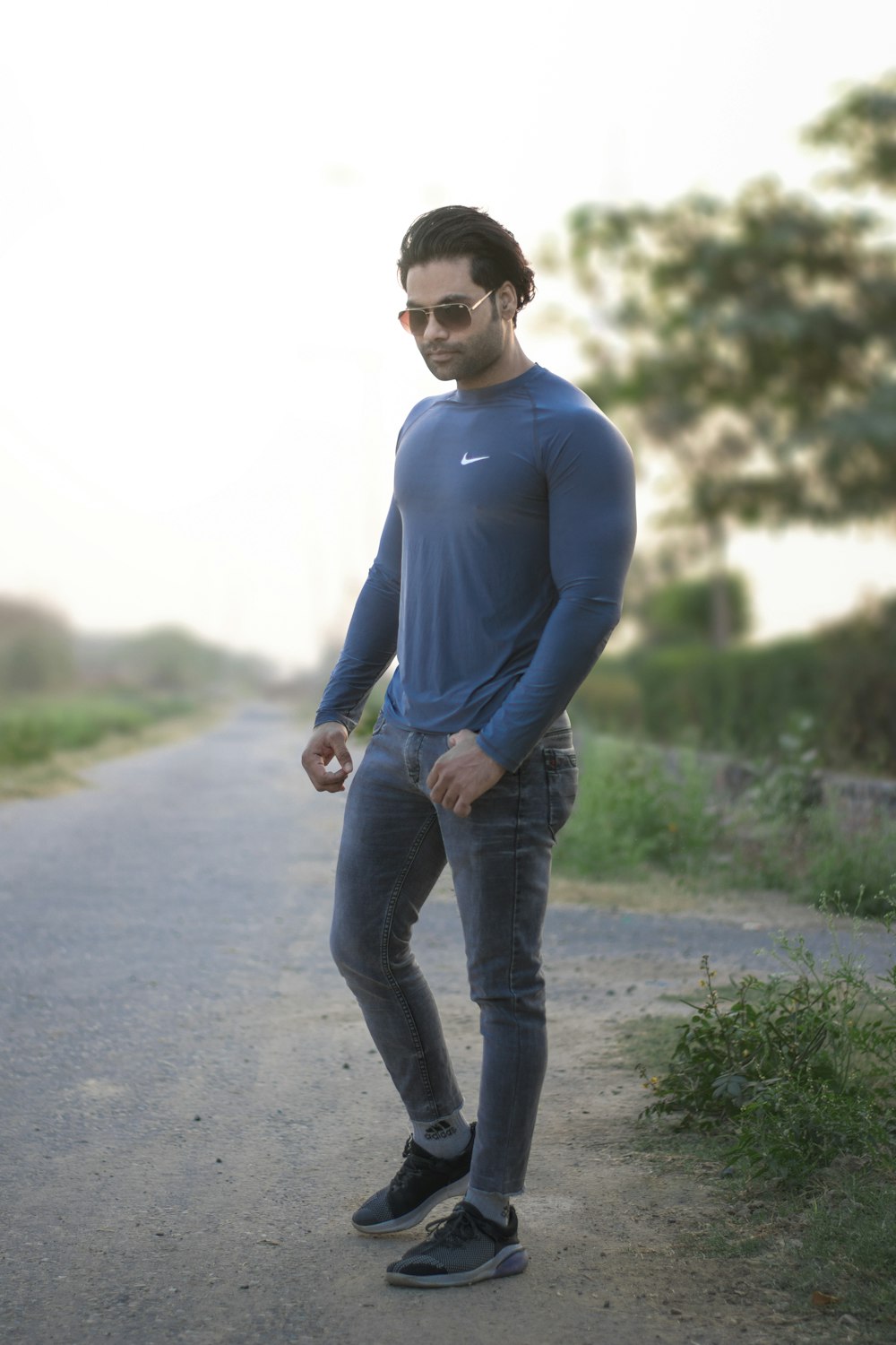 man in blue long sleeve shirt and blue denim jeans standing on road during daytime