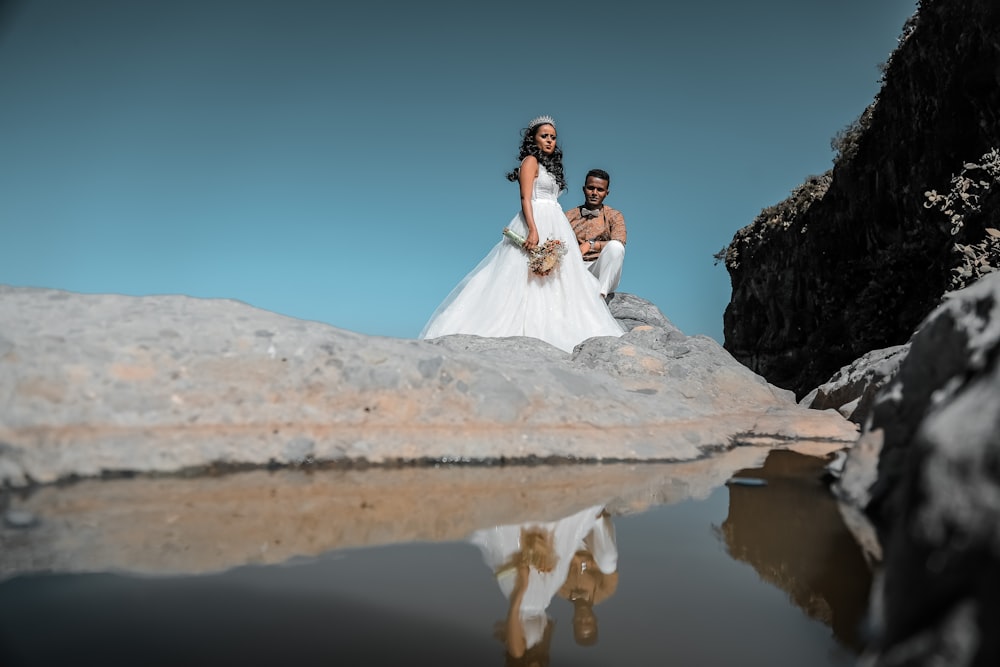 woman in white wedding gown standing on brown rock near body of water during daytime