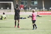 2 boys in red and black soccer jersey playing on green grass field during daytime