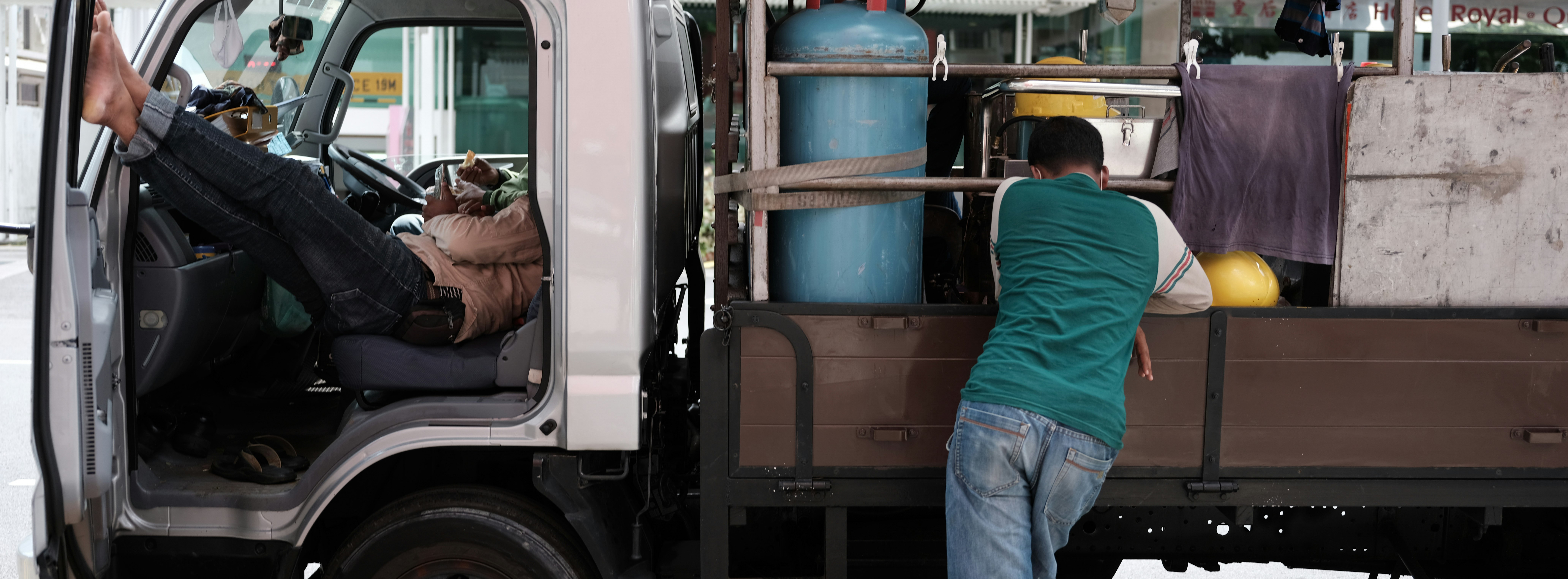 man in red shirt and blue denim jeans standing beside blue and black truck