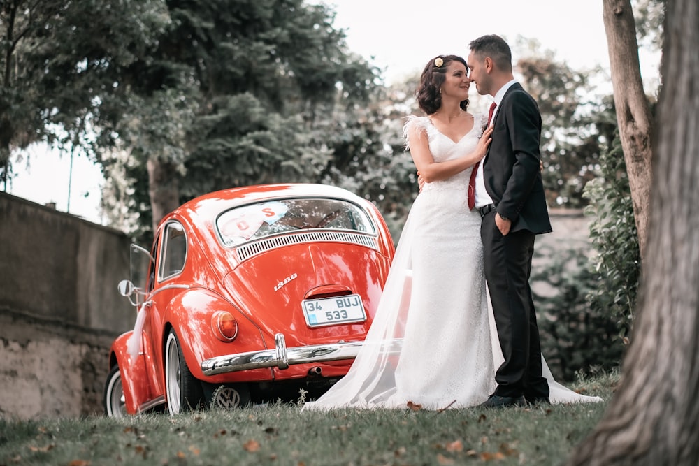 couple kissing beside red car during daytime