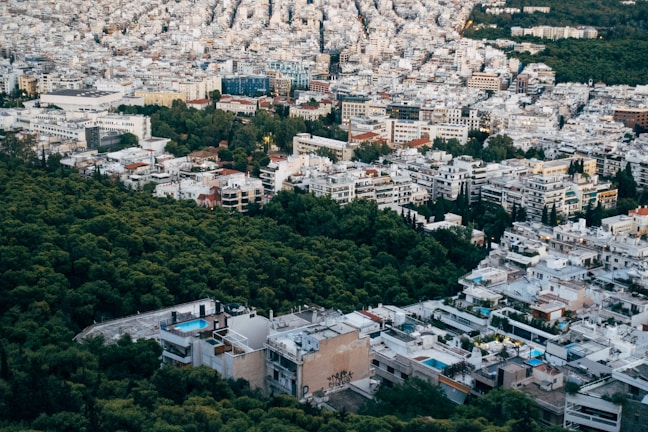 An urban landscape with a dense cluster of buildings interspersed with trees, capturing a blend of city architecture and green spaces. Some buildings have swimming pools on the rooftops, and the layout suggests a mix of residential and possibly commercial use.