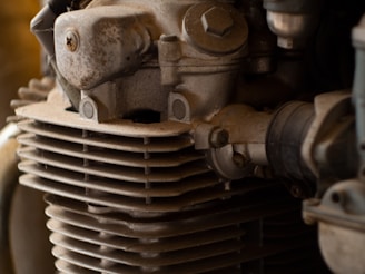 A close-up view of an engine component featuring a weathered, metallic surface with bolts and a series of horizontal cooling fins. The golden-brown hue suggests aging or exposure to environmental elements.