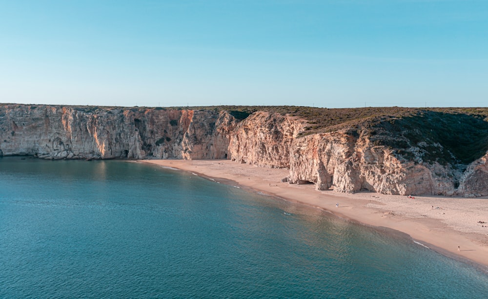 brown rocky mountain beside blue sea under blue sky during daytime