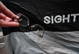 A hand holding a pair of eyeglasses, with a background featuring a black and white fabric with the word 'SIGHT' printed on it.