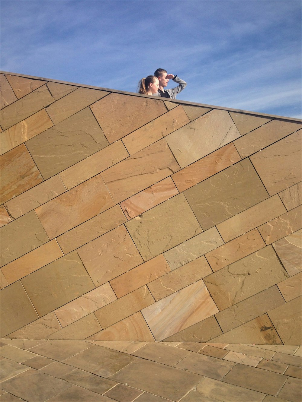 man in black t-shirt and blue denim jeans sitting on brown concrete wall during daytime