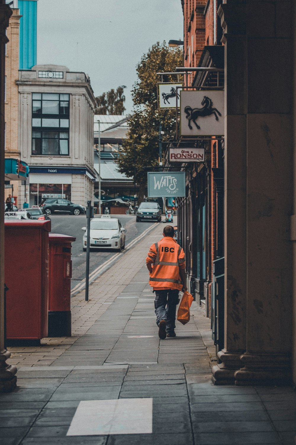 homem na jaqueta laranja andando na calçada durante o dia