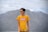 man in blue crew neck t-shirt standing near mountain under white clouds during daytime