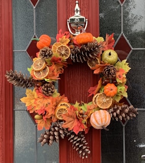 A vibrant autumn door swag hung on a rustic wooden door, bursting with fall hues.