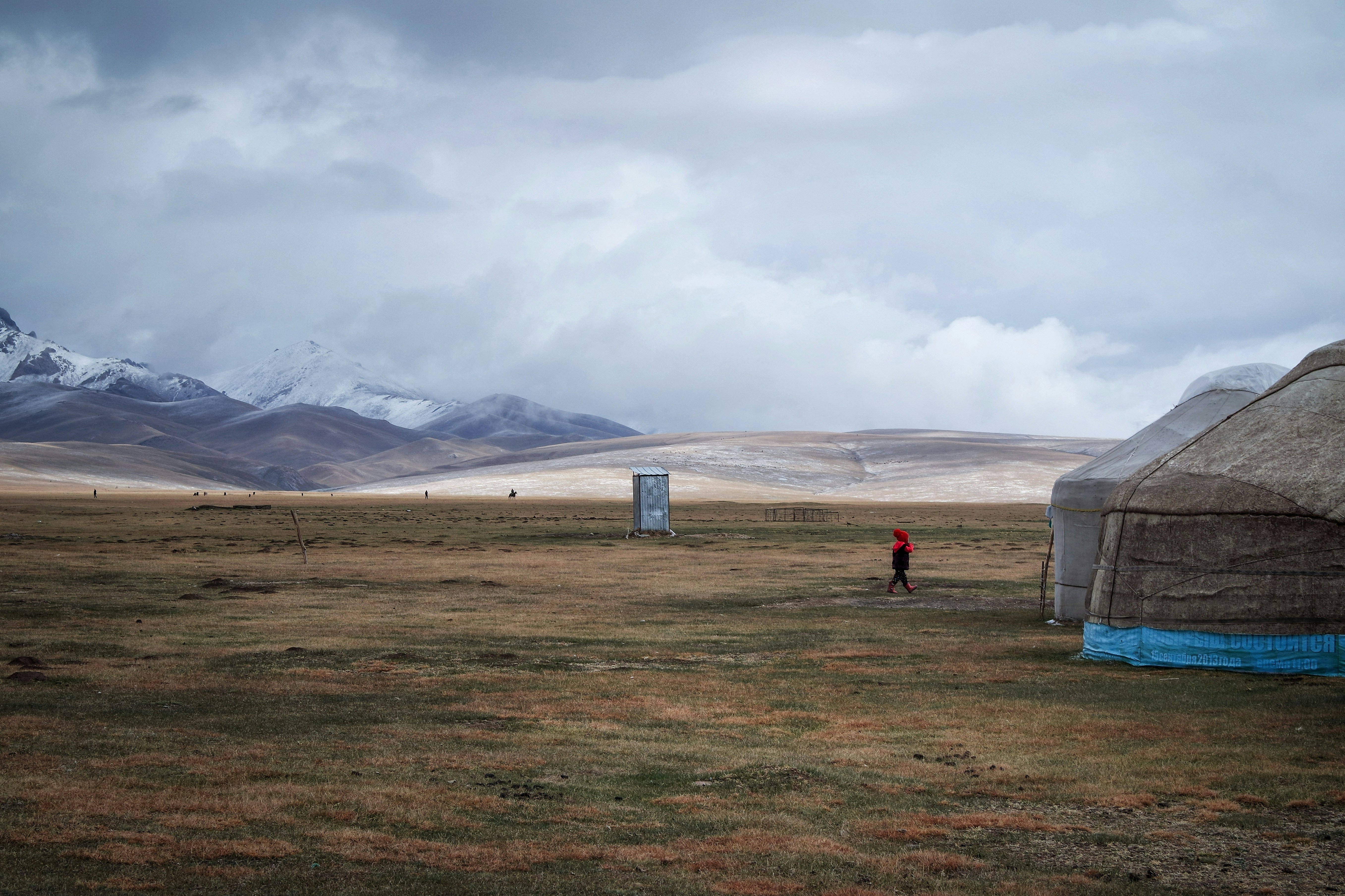 white tent on green grass field during daytime, A young girl crosses the open fields to her yurt at Song-Kul lake, Kyrgyzstan