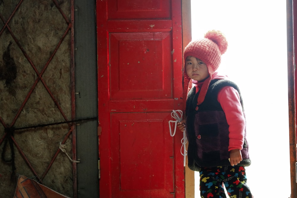 赤い木製のドアのそばに立つ赤と青のジャケットを着た少年