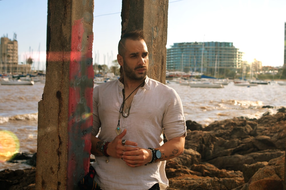 man in white polo shirt standing beside brown wooden post during daytime