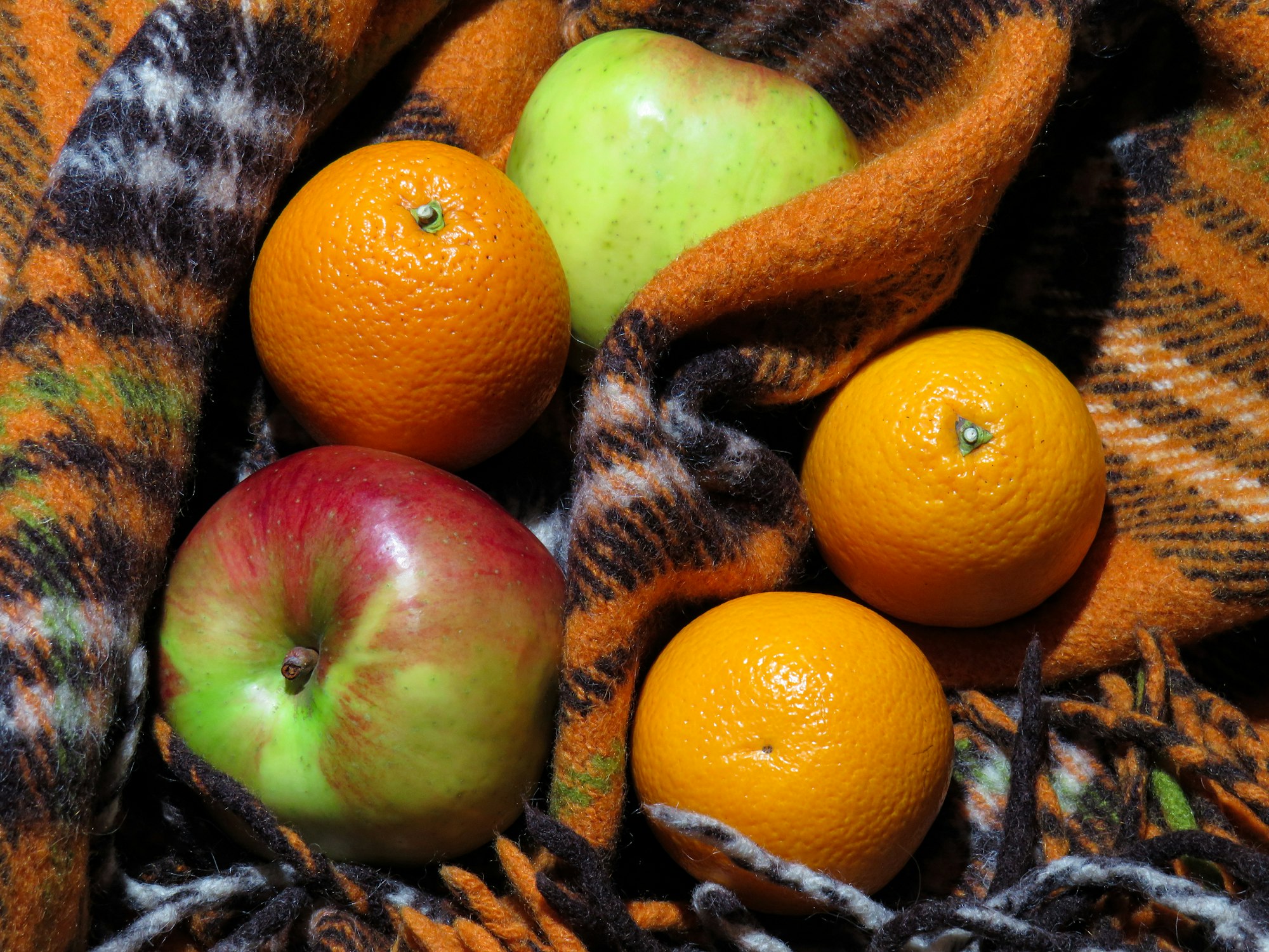 A warm plaid and tasty oranges and apples.