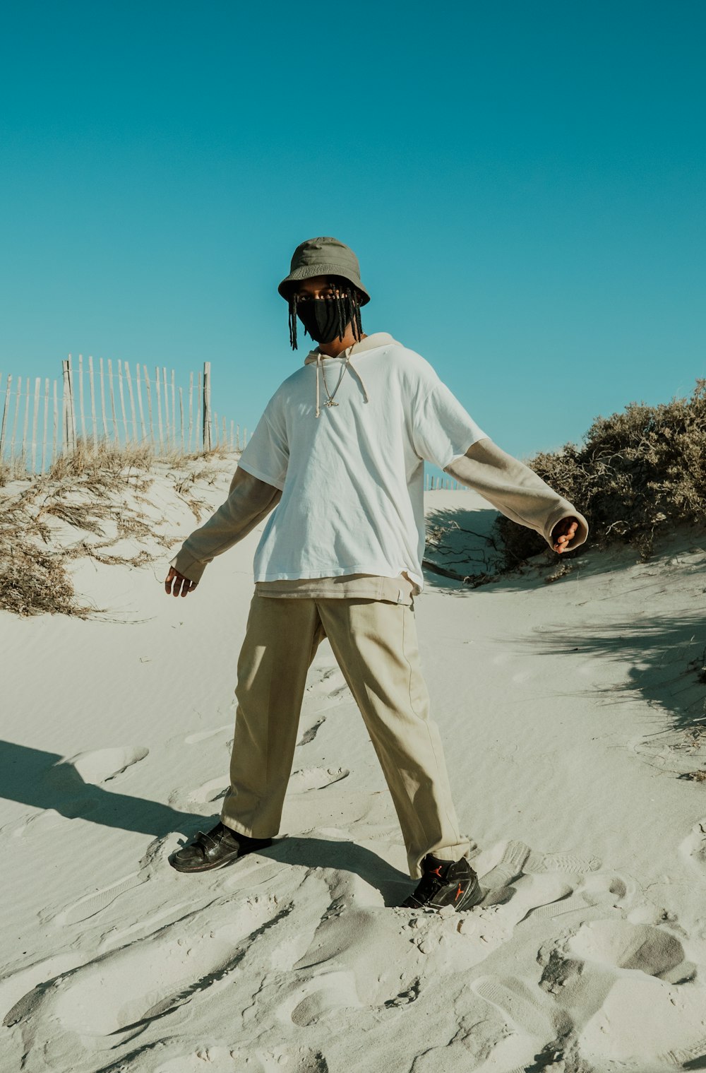 homme en chemise blanche et pantalon blanc debout sur le sable blanc pendant la journée