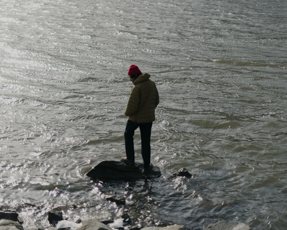 uomo in felpa con cappuccio gialla in piedi sull'acqua durante il giorno