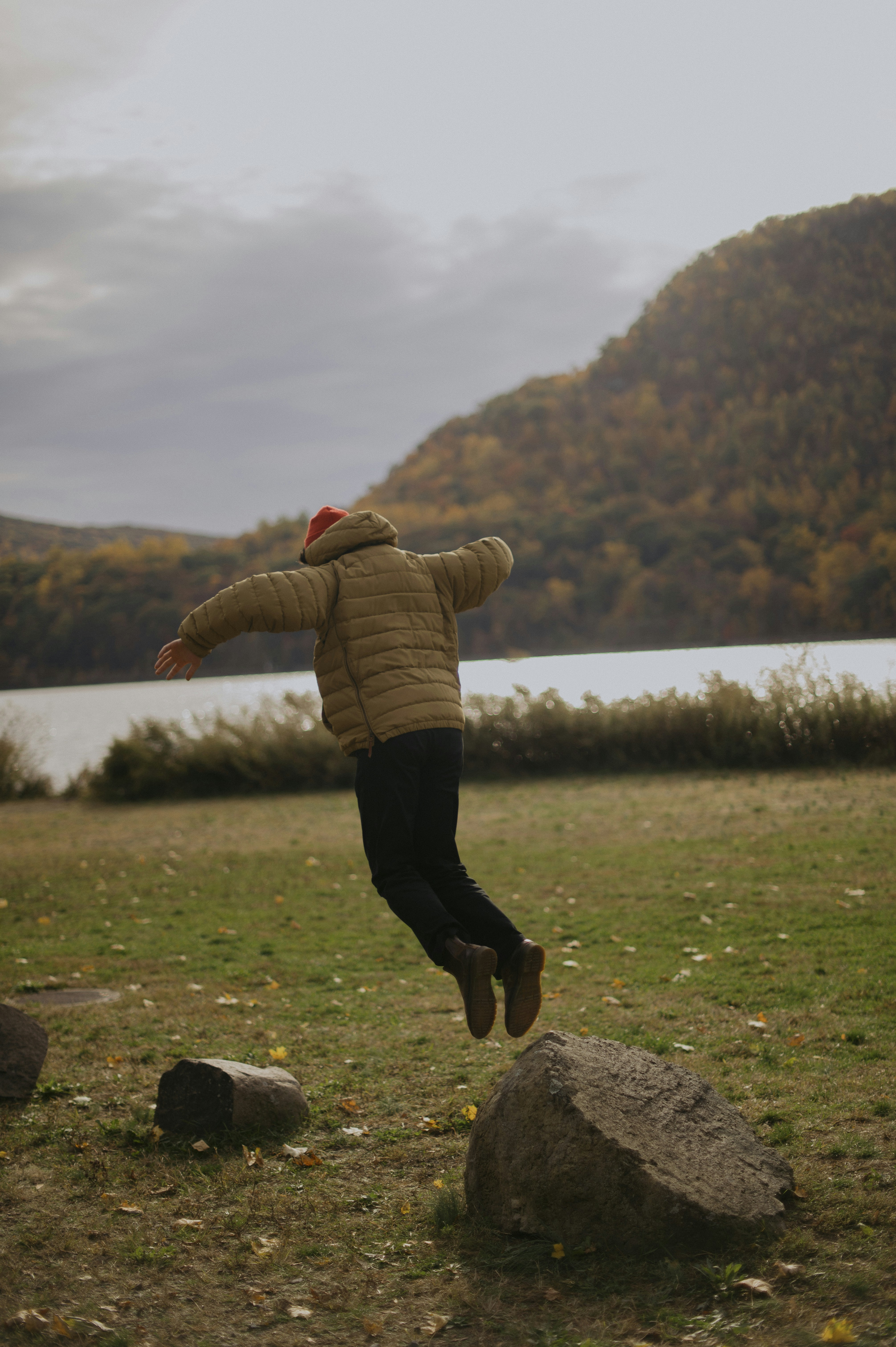 woman in brown jacket and black pants sitting on rock during daytime