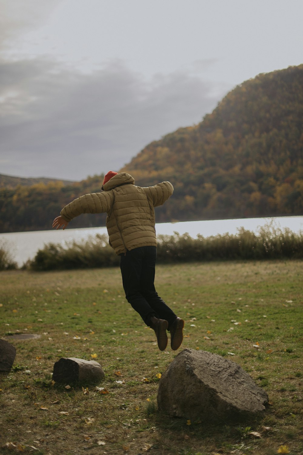 woman in brown jacket and black pants sitting on rock during daytime