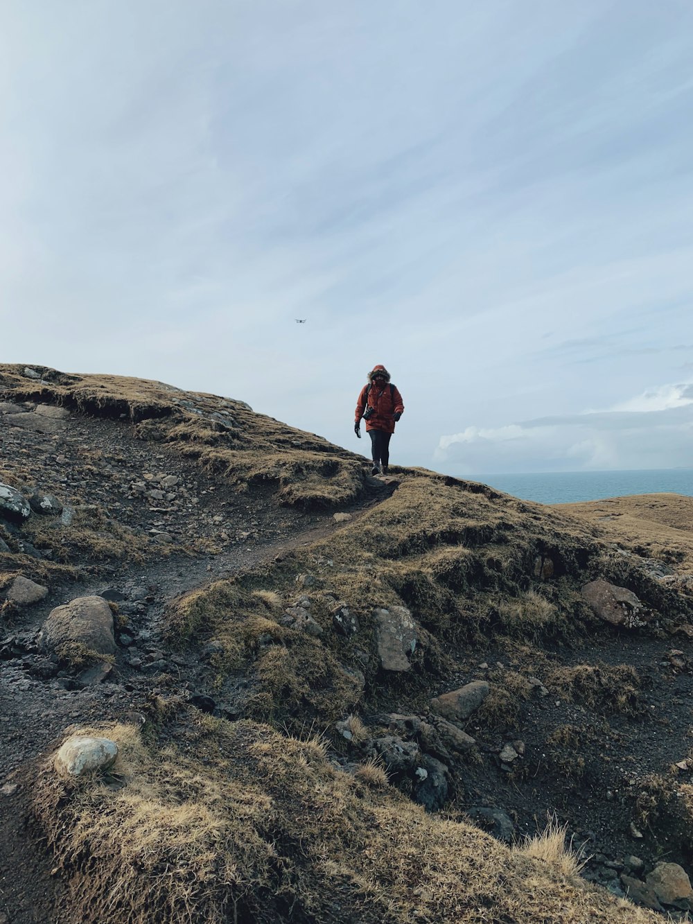 person in red jacket standing on brown rock formation under white clouds during daytime