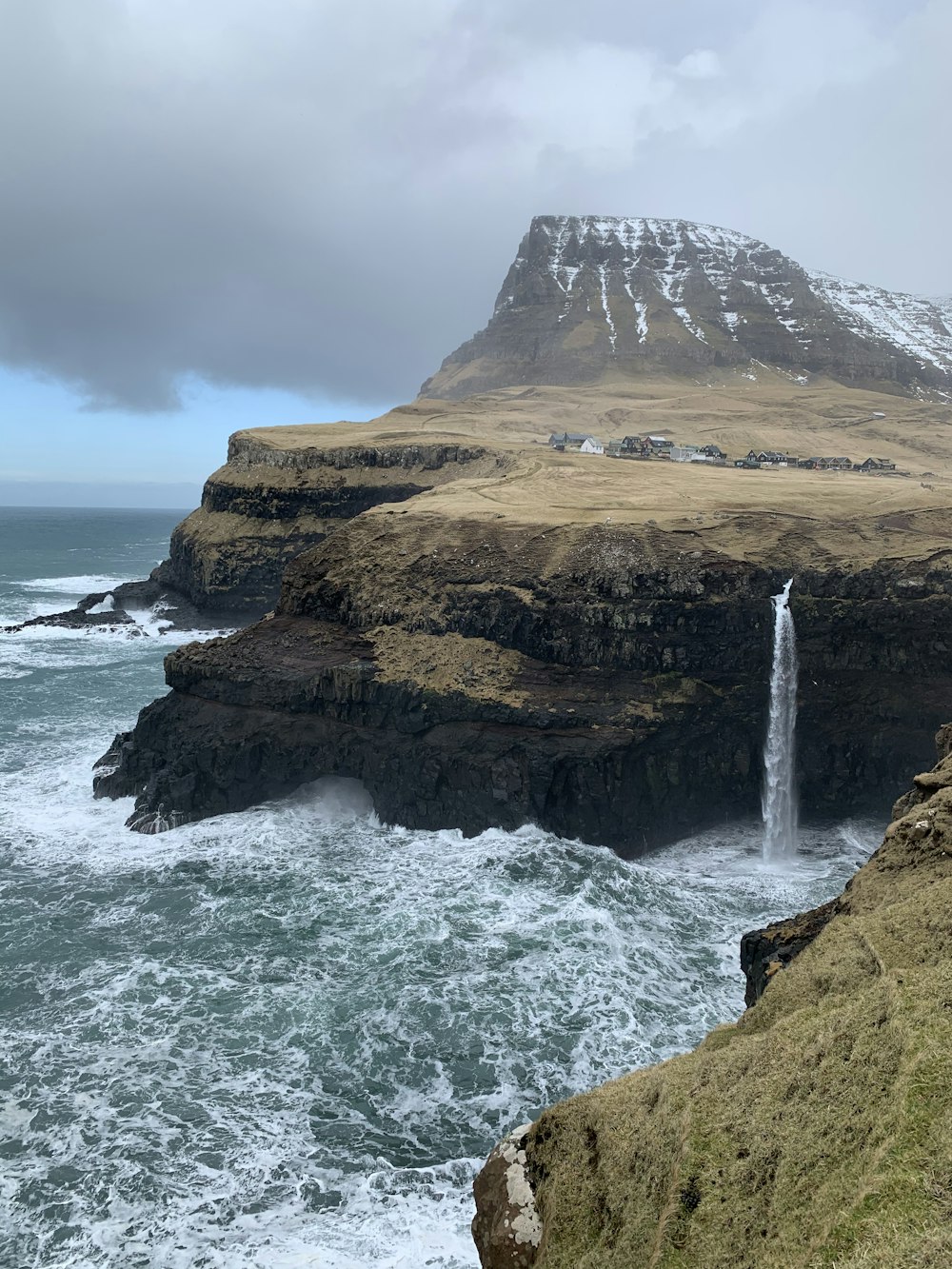 brown rock formation on sea under gray sky