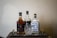 A selection of three liquor bottles arranged on a wooden tray with a crystal whiskey glass placed in front. The bottles include Jim Beam Double Oak, Kraken, and Winchester Bourbon Whiskey. The scene is set against a plain textured wall, giving a classic and refined appearance.