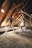 Two dancers perform in an attic with rustic wooden beams and a slanted roof. Light filters through small windows, illuminating their intricate choreography. The dancers display grace and balance amidst the aged, textured setting.