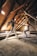 Two dancers perform in an attic with rustic wooden beams and a slanted roof. Light filters through small windows, illuminating their intricate choreography. The dancers display grace and balance amidst the aged, textured setting.