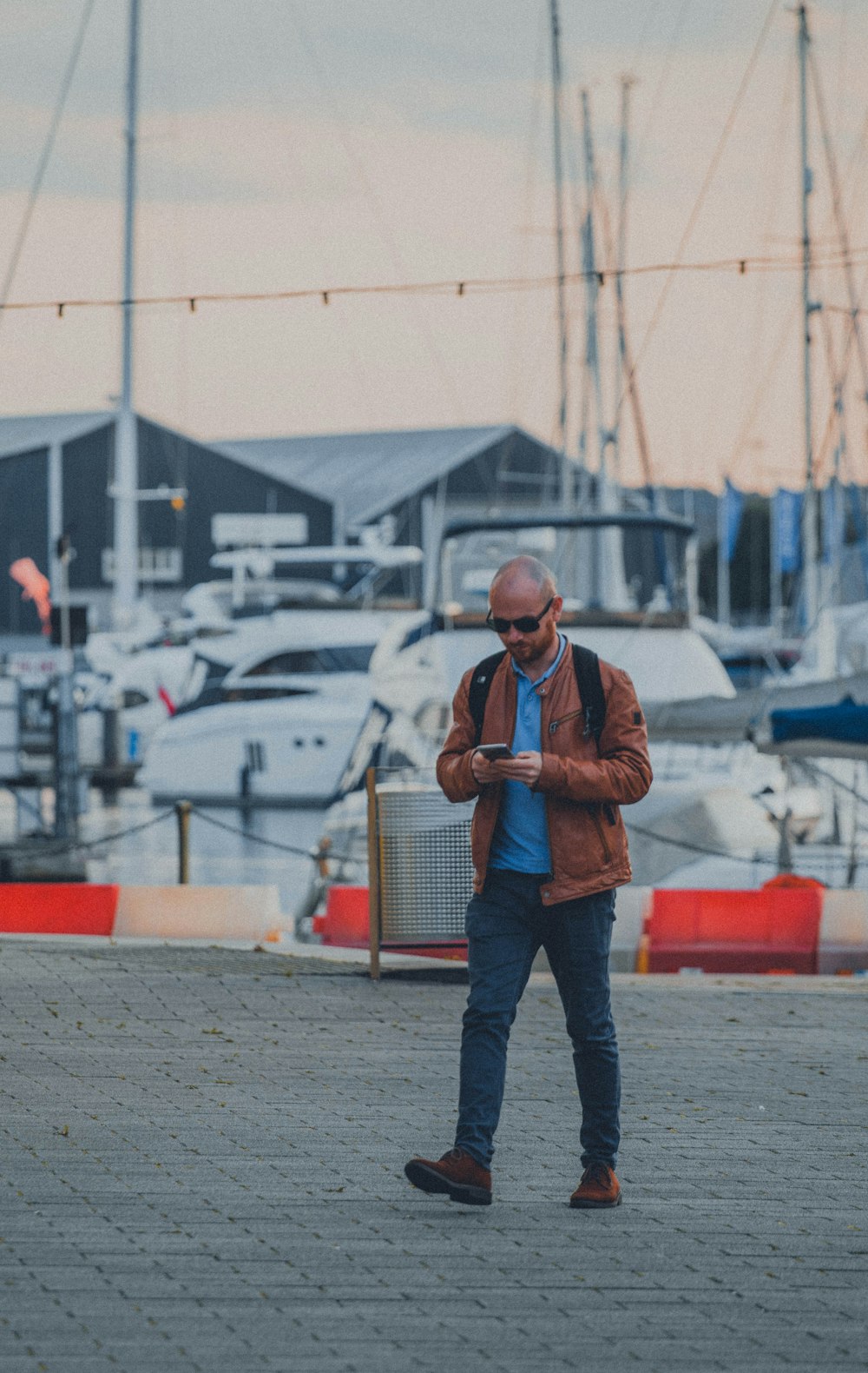 man in brown vest and blue denim jeans standing on gray concrete pavement during daytime