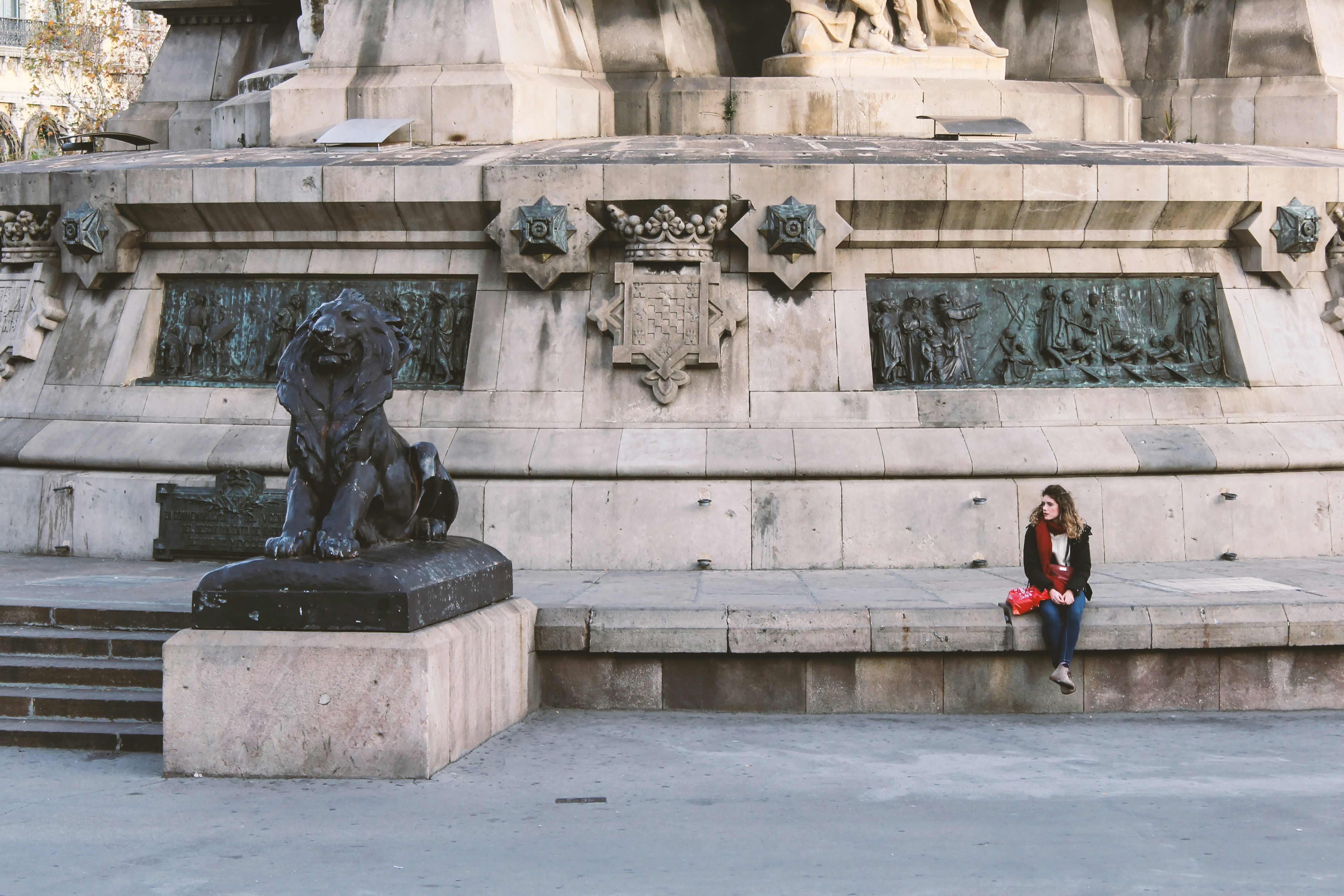 woman in red jacket standing near gray concrete statue during daytime