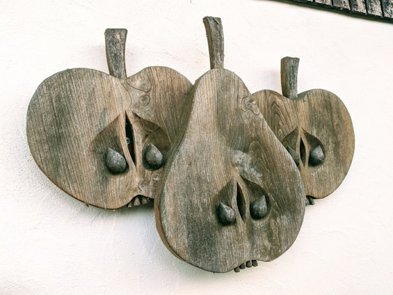 A wooden wall sculpture features three stylized pear-like shapes with textures resembling natural wood grain. Each shape includes carved details like leaves and seeds, creating an abstract and artistic appearance.