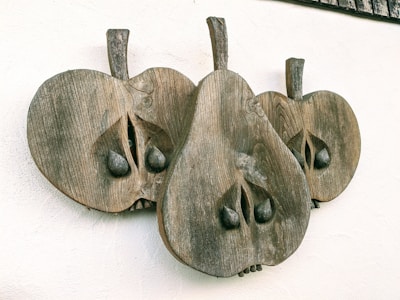 A wooden wall sculpture features three stylized pear-like shapes with textures resembling natural wood grain. Each shape includes carved details like leaves and seeds, creating an abstract and artistic appearance.