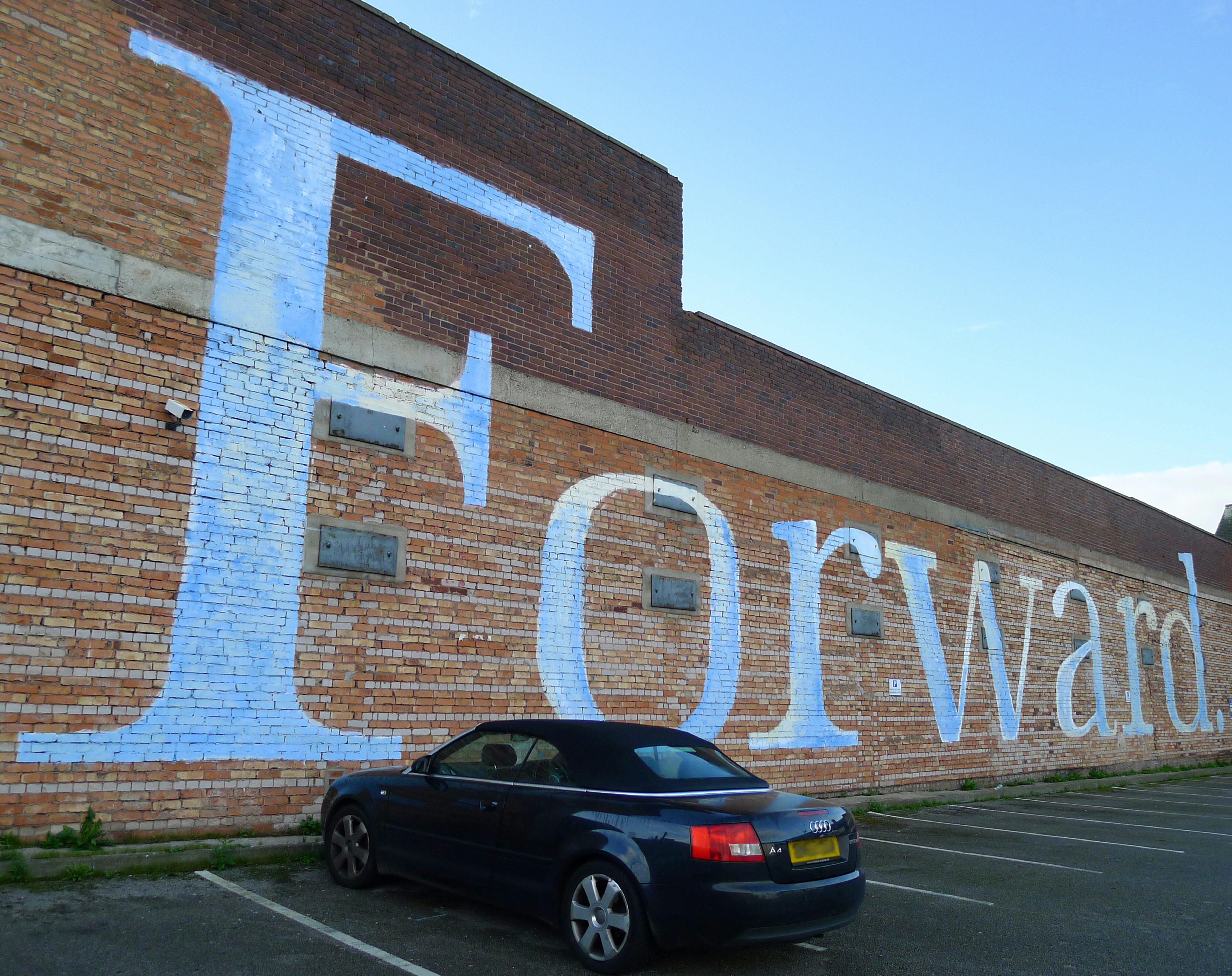 black sedan parked beside brown brick building during daytime