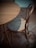 A wooden chair with a woven cane seat is positioned next to a round wooden table. The flooring features a herringbone pattern, and the lighting creates soft shadows.