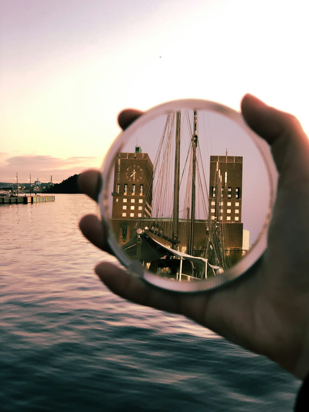 person holding round mirror reflecting body of water during daytime