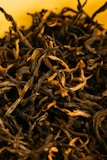 Close-up of deep amber black tea leaves with hints of dried petals.