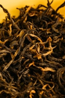 Close-up of premium Assam CTC tea leaves in a rustic wooden bowl.