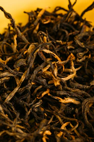 Close-up of rich, dark black tea leaves spilling from a rustic ceramic bowl.
