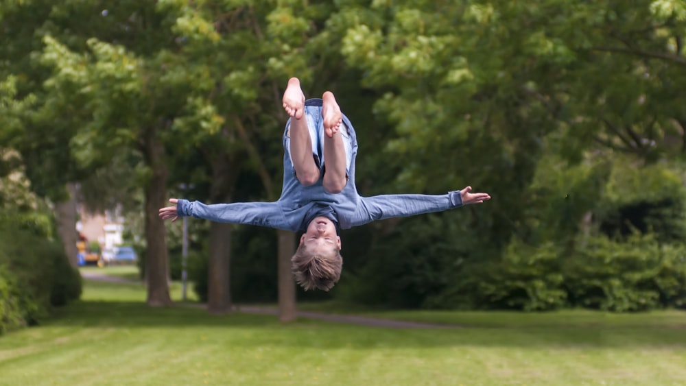 woman in blue tank top and blue denim jeans jumping on green grass field during daytime