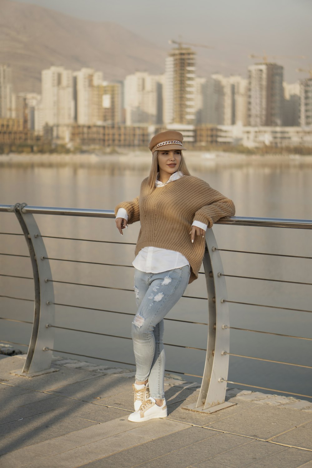 woman in brown long sleeve shirt and blue denim jeans leaning on gray metal railings