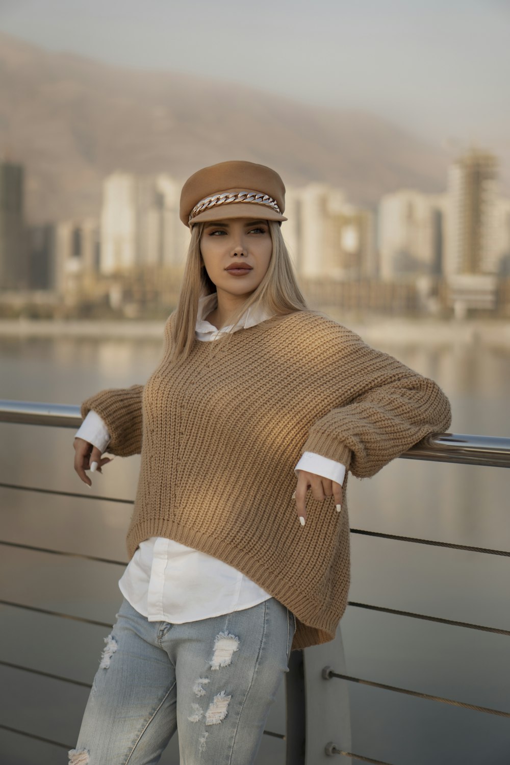 woman in brown knit sweater and white denim jeans standing beside railings during daytime