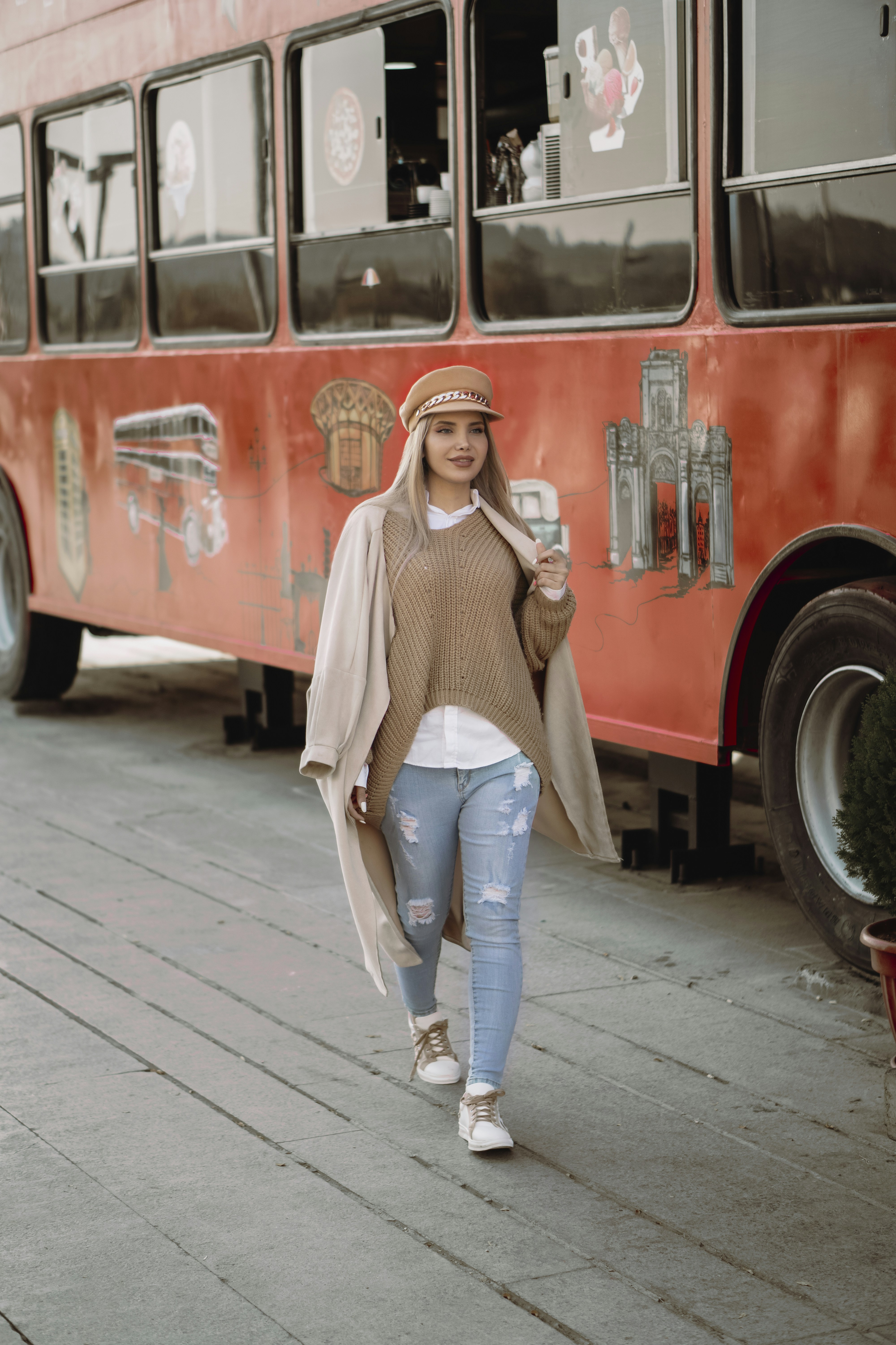 wanita dengan sweater rajutan putih dan jeans denim biru berdiri di samping bus merah