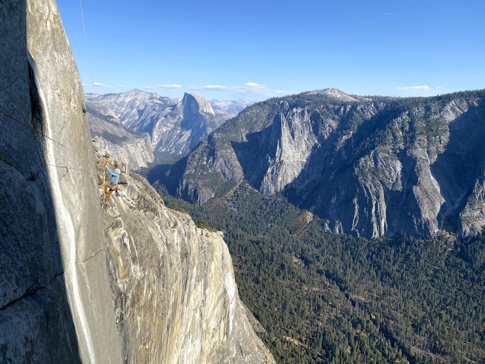 person in orange jacket and blue denim jeans standing on gray rock mountain during daytime