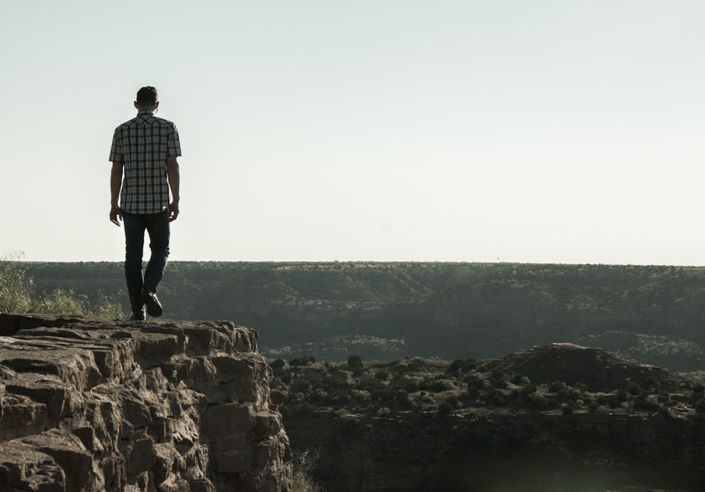 man in white and black checkered dress shirt standing on brown rock formation during daytime