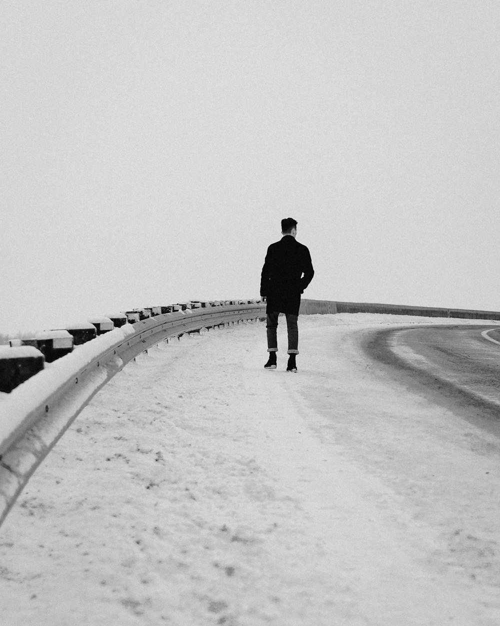 Hombre en chaqueta negra caminando en el camino cubierto de nieve durante el día