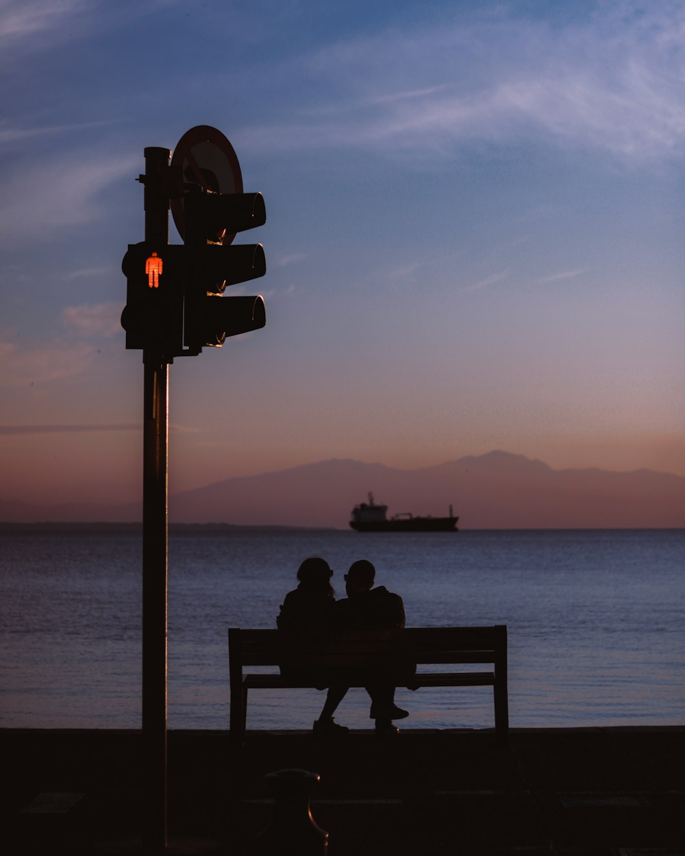 silhouette of person sitting on bench near body of water during sunset