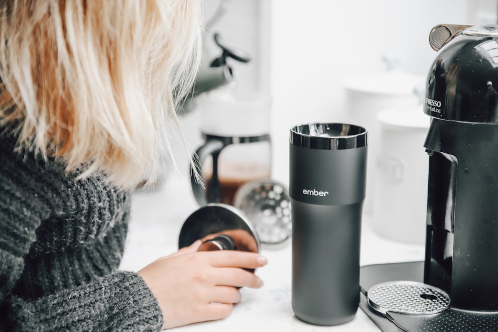 woman in gray sweater holding silver and black travel mug